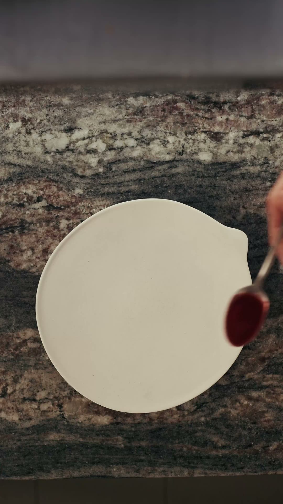 Assiette blanche sur un plan de travail en granit, cuillère de coulis de fraise